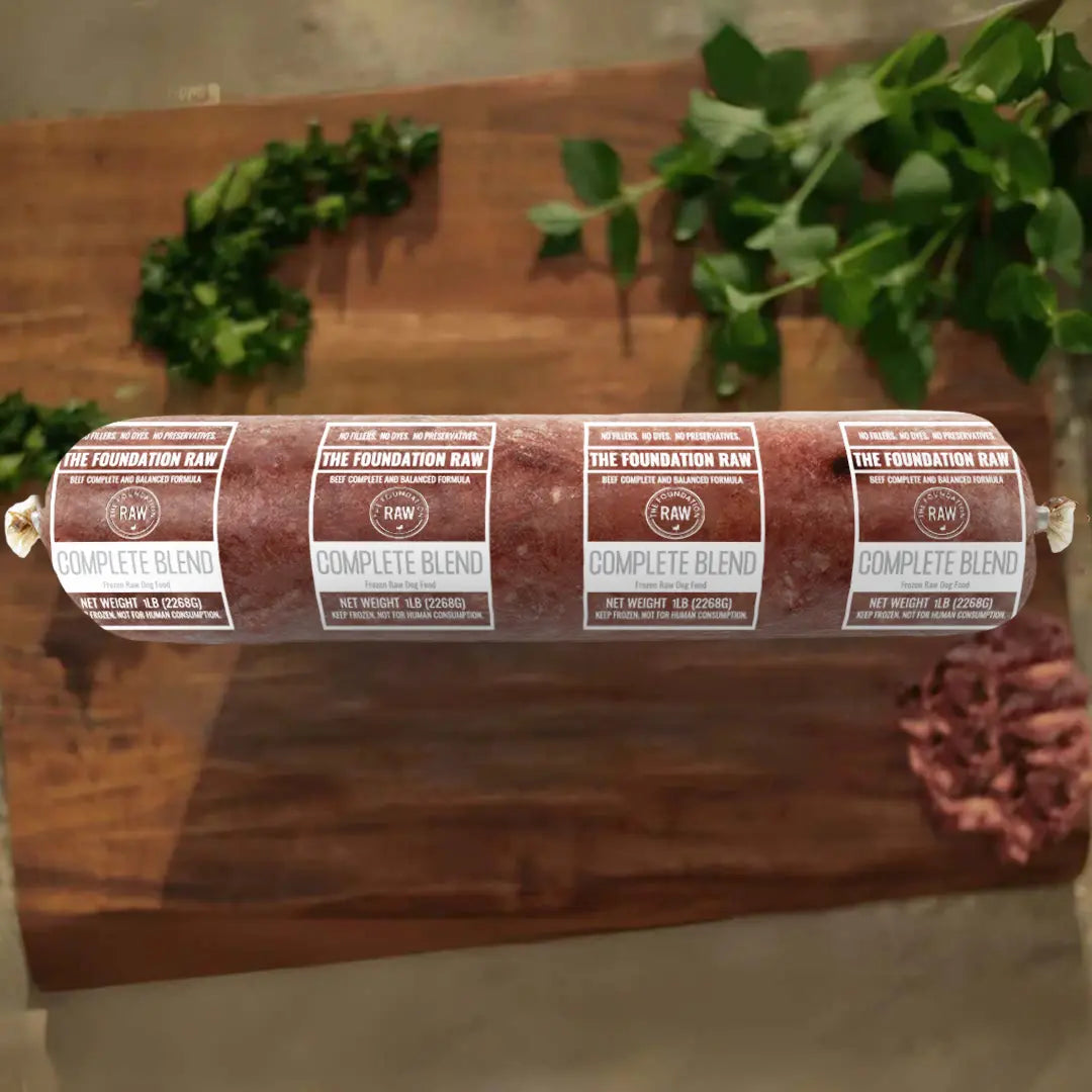 complete blend raw dog food, a rolled meat product with labels on a wooden surface, greenery in the background