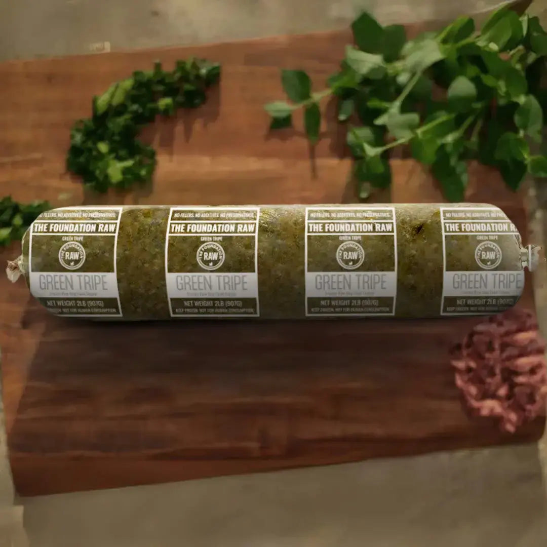 The Foundation Raw' s Rolled-up green tripe frozen raw dog food on a wooden surface with plants in the background.