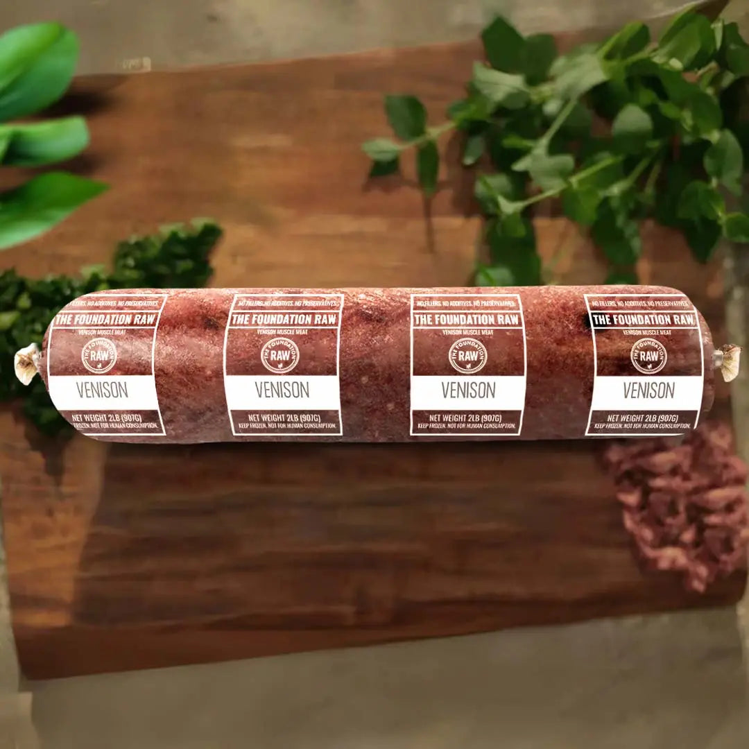 Rolled venison meat with labels on a wooden surface, greenery in the background