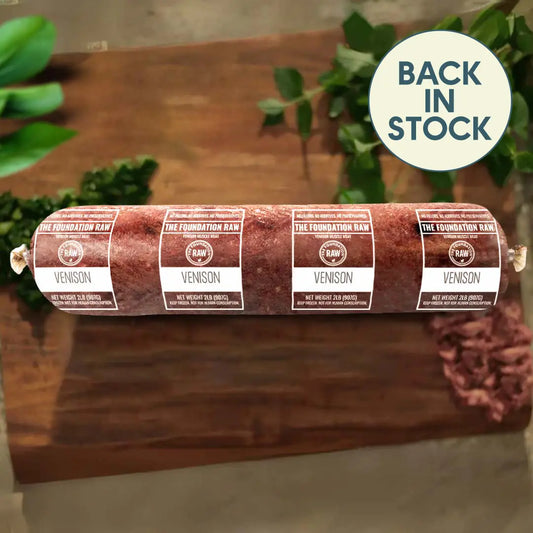 Rolled venison sausage with labels on a wooden board, greenery in the background