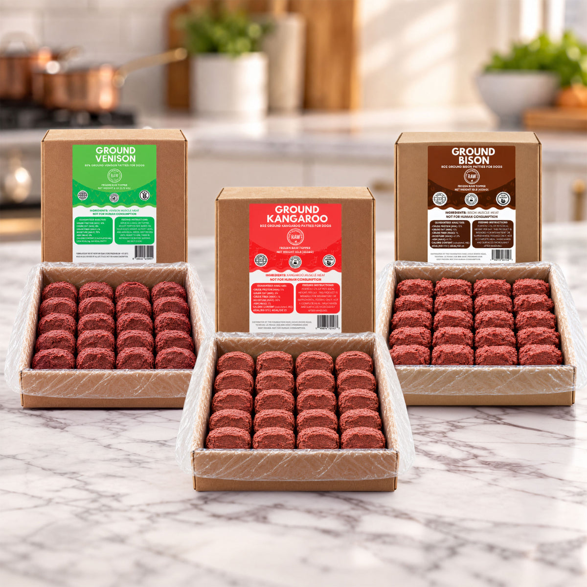 Three open cardboard boxes of ground meat patties arranged on a marble countertop in a kitchen setting. The center box is labeled Ground Kangaroo, flanked by Ground Venison and Ground Bison boxes behind it.