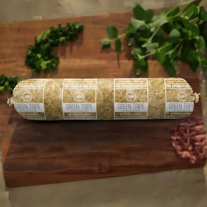The Foundation Raw' s Rolled-up green tripe frozen raw dog food  on a wooden surface with plants in the background.