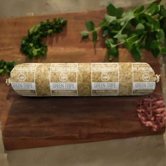 The Foundation Raw' s Rolled-up green tripe frozen raw dog food  on a wooden surface with plants in the background.